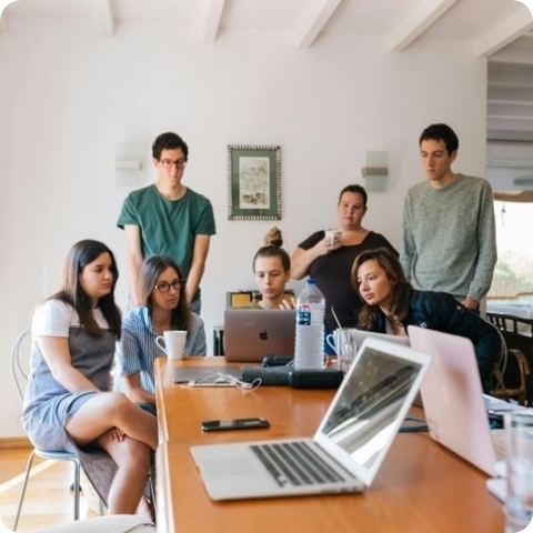a group of people at a table gathering around a laptop