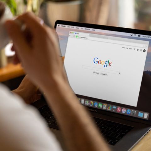 a person drinking coffee, searching Google on their laptop