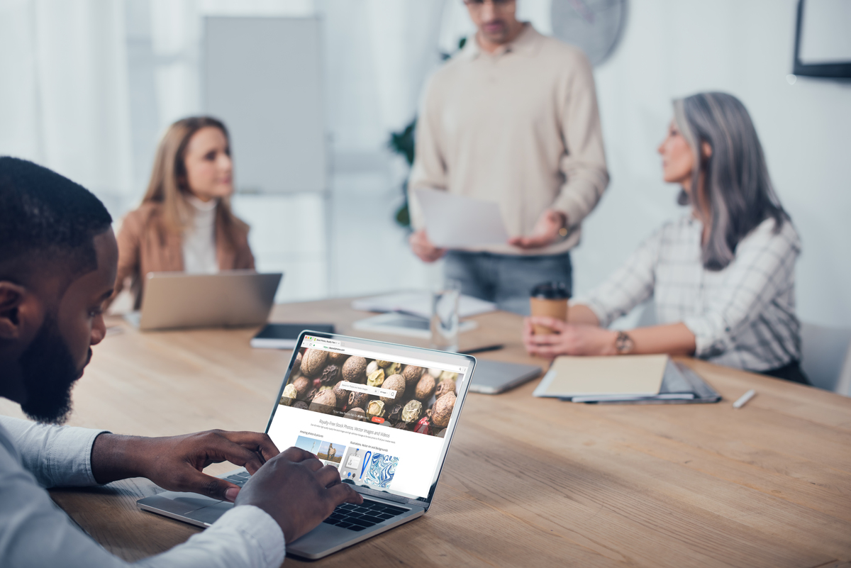 four professionals sitting at a table. One has his laptop open an is looking at a website