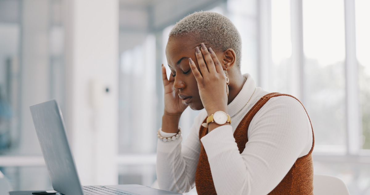 woman with hands on her temples, eyes closed in front of her computer